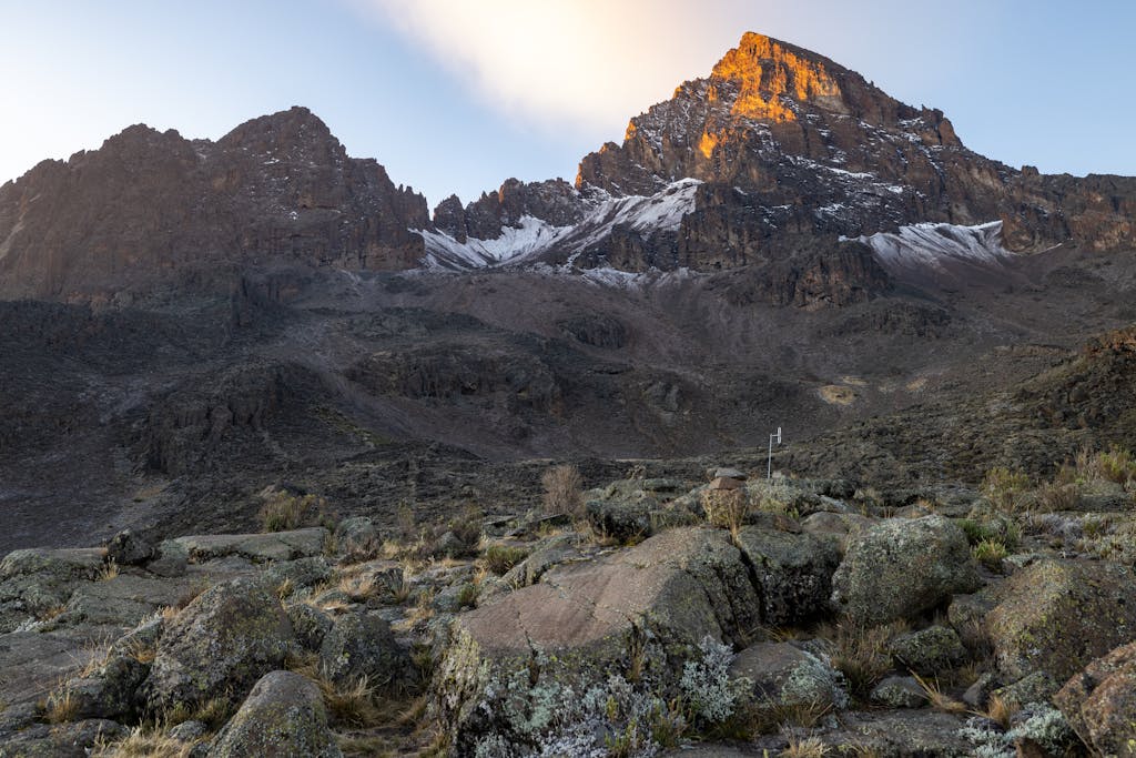 Stunning view of Mount Kilimanjaro's peak at sunrise, showcasing rocky terrain and snow patches.